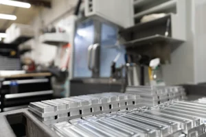 Stacks of precision-milled aluminum parts on a tray in a CNC machine shop with vertical machining centers in the background — Dallas Precision Machining.